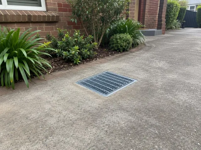 Outdoor driveway drain grate beside brick house and garden bed in Cremorne