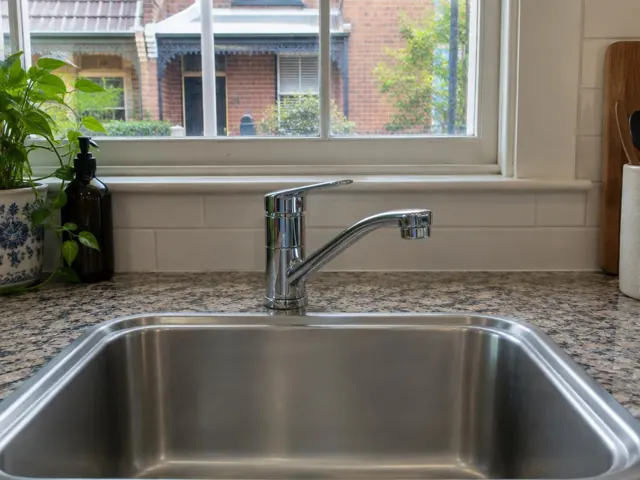 Chrome kitchen mixer tap above stainless sink and speckled benchtop by a window in North Sydney
